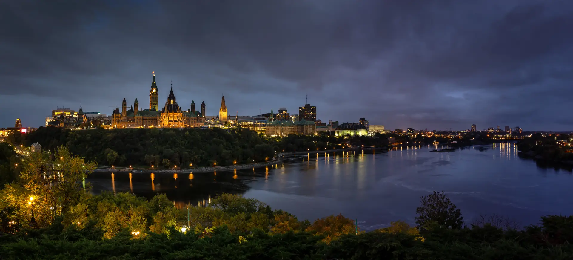 Parliament Hill and downtown Ottawa lit up at dusk, seen across the Ottawa River